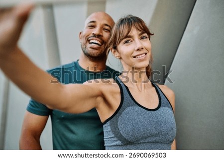 Young couple taking a selfie while posing against a wall after workout in athletic wear at urban location