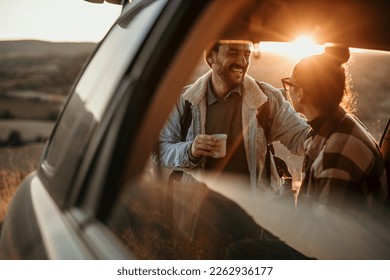Young couple talking, drinking a coffee watching the sunset from their car. Couple travel concept - Powered by Shutterstock