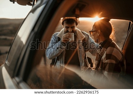 Young couple talking, drinking a coffee watching the sunset from their car. Couple road travel together