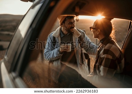 Young couple talking, drinking a coffee watching the sunset from their car.