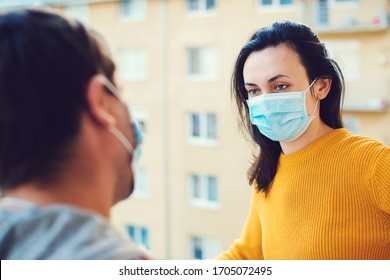 Young couple are talking on balcony outside. Home isolation during coronavirus quarantine. Man and woman wearing face mask. Coronavirus protection and prevention. Stay home. Couple standing on balcony - Powered by Shutterstock