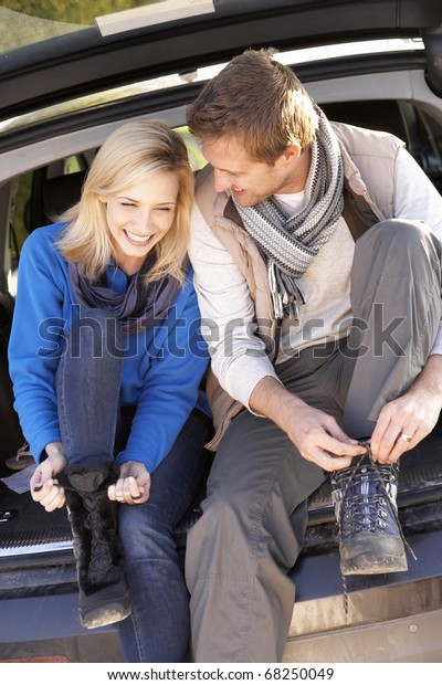 Young couple tie boots at\
rear of car
