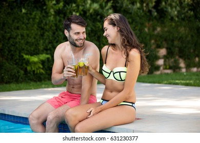 Young couple toasting glasses of iced tea at poolside on a sunny day - Powered by Shutterstock