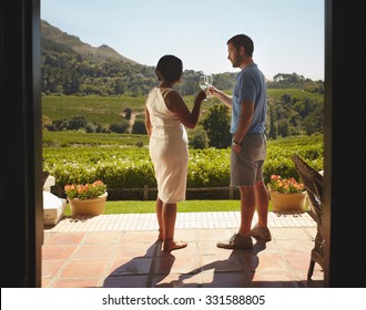 Young Couple Toasting Wine While Standing Outdoors At Winery Restaurant Patio. Man And Woman On Vacation Celebrating With Wine.