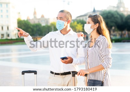 Young couple of tourists in disposable face masks admiring city views while traveling together. Easing coronavirus lockdown concept

