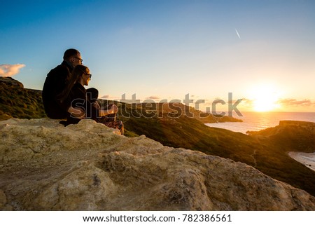 Young couple of tourists on beautiful Ghajn Tuffieha Bay taken during colorful sunset on Malta island. Beautiful landscape in south Europe.