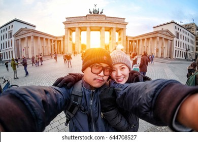 Young Couple Tourists Selfie With Smartphone At Brandenburger Gate In Sunlight, The Famous Landmark Of Berlin, Germany