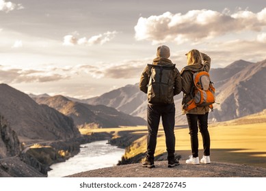 Young couple of tourists is standing with backpacks in mountains and enjoys nice view at sunset and big river - Powered by Shutterstock