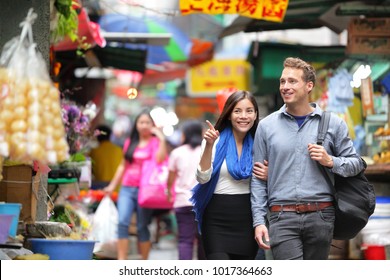 Young Couple Tourists Walking Shopping In Street Food Market In Hong Kong. Couple Looking Around At Stand Shops. Asian Woman, Caucasian Man Interracial People.