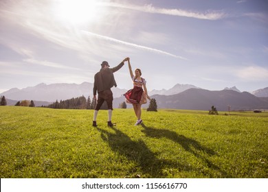 Young Couple In Traditional Bavarian Clothes With Girl In Dirdl Dress Dance In Nature / Bavarian Couple Dance Oktoberfest Munich 