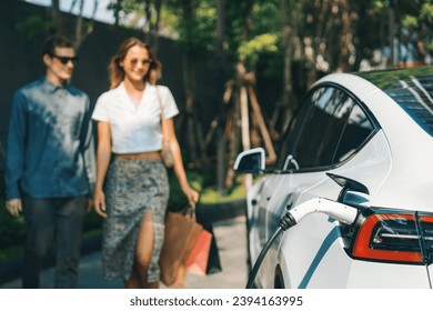 Young couple travel with EV electric car charging in green sustainable city outdoor garden in summer shows urban sustainability lifestyle by green clean rechargeable energy of electric vehicle innards - Powered by Shutterstock