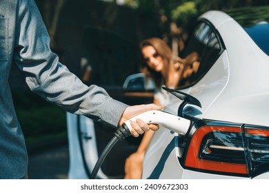 Young couple travel with EV electric car charging in green sustainable city outdoor garden in summer shows urban sustainability lifestyle by green clean rechargeable energy of electric vehicle innards - Powered by Shutterstock