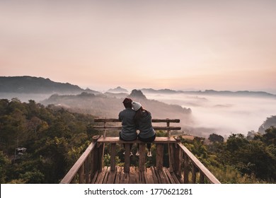 Young couple traveler looking at sea of mist and sunset over the mountain at Mae Hong Son, Thailand