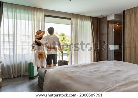 Young couple traveler opening the curtains and looking at the view from the window of a hotel room while on summer vacation, Travel lifestyle concept