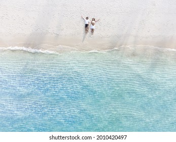 Young couple traveler sitting and relaxing at beautiful tropical white sand beach with wave foam and transparent sea, Summer vacation and Travel background Top view from drone - Powered by Shutterstock