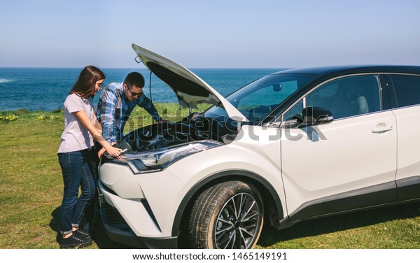 Young couple tries to fix the broken down car near\
the coast