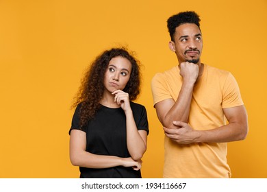 Young couple two american friends together family pensive thoughtful dreamful man african woman 20s in yellow black t-shirt proping up chin looking aside isolated on orange background studio portrait