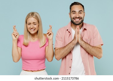 Young couple two friends family man woman in casual clothes waiting for special moment, keeping fingers crossed, prayer gesture together isolated on pastel plain light blue color background studio.
