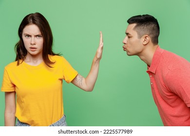Young couple two friends family man woman wear basic t-shirts together man try want kiss woman but she do stop palm gesture and does not want it isolated on pastel plain light green color background