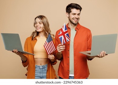 Young couple two friends family IT man woman wear casual clothes looking camera use work on laptop pc computer hold American British flag together isolated on pastel plain light beige color background - Powered by Shutterstock