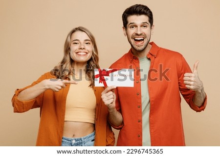 Young couple two friends family man woman wear casual clothes looking camera together hold point on gift certificate coupon voucher card for store isolated on pastel plain light beige color background