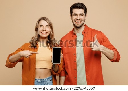 Young couple two friends family man woman wear casual clothes hold in hand use mobile cell phone with blank screen workspace area show thumb up together isolated on pastel plain light beige background
