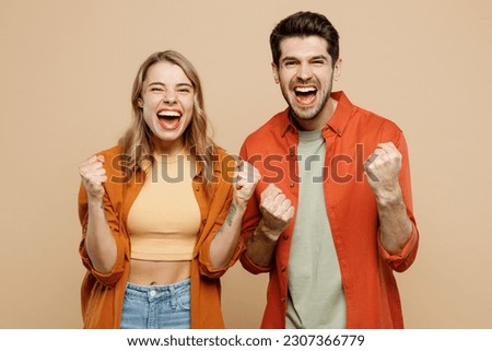 Young couple two friends family man woman wear casual clothes looking camera together do winner gesture celebrate clenching fists say yes isolated on pastel plain light beige color background studio