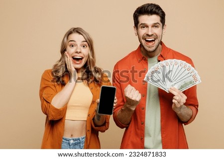 Young couple two friends family man woman wear casual clothes hold in hand fan of cash money in dollar banknotes use mobile cell phone together isolated on pastel plain light beige background studio