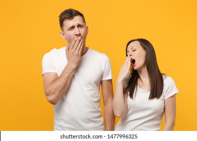 Young couple two friends guy girl in white empty blank design t-shirts posing isolated on yellow orange background. People lifestyle concept. Mock up copy space. Yawning, covering mouth with hands - Shutterstock ID 1477996325
