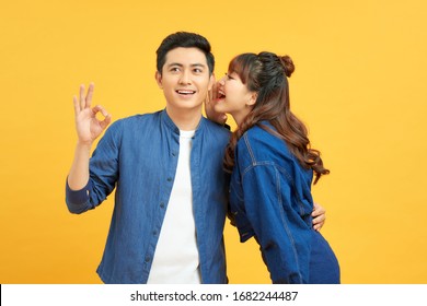 Young Couple Two Friends Guy Girls Posing Isolated On Yellow Orange Wall Background. People Lifestyle Concept. Mock Up Copy Space. Whispering Secret Behind Hand