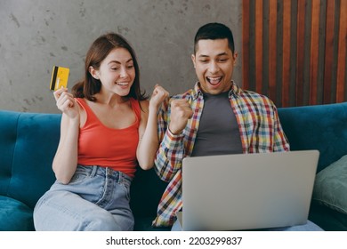 Young Couple Two Friends Man Woman Wear Casual Clothes Use Mobile Cell Phone Credit Bank Card Shopping Online Book Tour Sit On Sofa Together Stay Home Flat Rest Spend Spare Time In Living Room Indoor