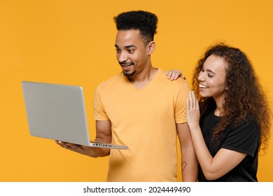 Young Couple Two Friends Together Family African Man Woman 20s Wearing Black T-shirt Holding Using Laptop Pc Computer Chatting In Social Network Isolated On Yellow Color Background Studio Portrait