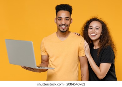 Young Couple Two Friends Together Family African Freelancer Man Woman 20s Wearing Black T-shirt Holding Using Laptop Pc Computer Working Online Hug Isolated On Yellow Color Background Studio Portrait