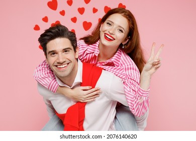 Young Couple Two Friends Woman Man In Casual Shirt Giving Piggyback Ride To Joyful, Sit On Back Show V-sign Isolated On Plain Pastel Pink Background. Valentine's Day Birthday Holiday Party Concept.