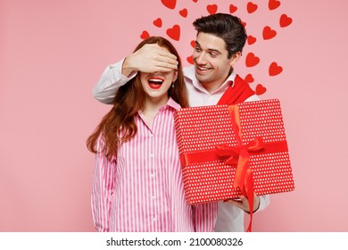 Young Couple Two Friends Woman Man 20s In Casual Shirt Give Red Present Box With Gift Ribbon Bow Cover Eyes Isolated On Plain Pastel Pink Background. Valentine's Day Birthday Holiday Party Concept.