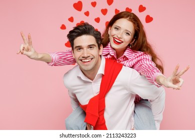 Young couple two friends woman man wear casual shirt giving piggyback ride to joyful sit on back show v-sign isolated on plain pastel pink background. Valentine's Day birthday holiday party concept.
