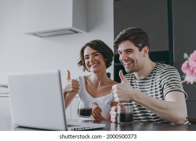 Young Couple Two Woman Man In Casual T-shirt Clothes Sit Table Drink Coffee Talk Zoom Video Call By Laptop Pc Computer Show Thumb Up Gesture In Light Kitchen At Home Together People Lifestyle Concept