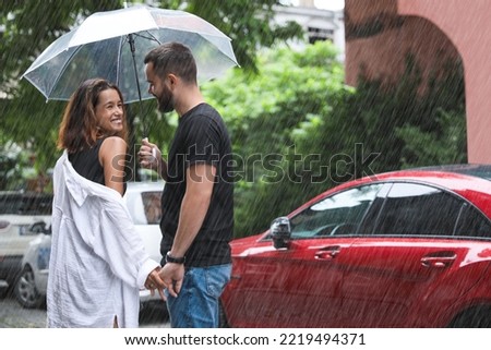 Young couple with umbrella enjoying time together under rain on city street, space for text