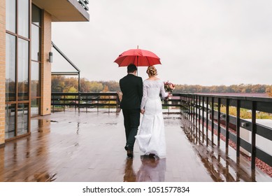 Young couple under umbrella in the autumn on rainy day weather, copy space. lovely couple in love with red umbrella walking along. Bride and groom walking away under an umbrella - Powered by Shutterstock