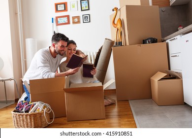 Young Couple Unpacking Cardboard Boxes At New Home.Moving House.Reading A Old Books.