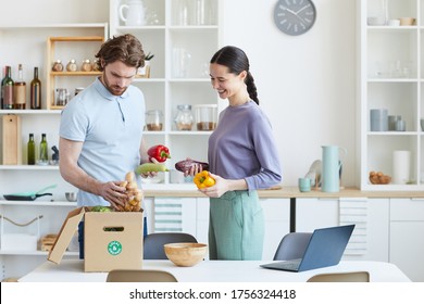 Young Couple Unpacking Food Together From The Cardboard Box After Shopping