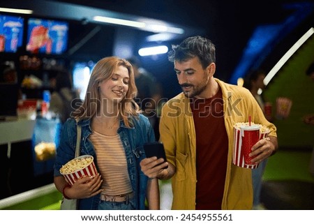 Young couple using app on mobile phone while going on movie projection in cinema. 