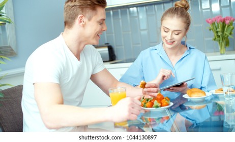 Young couple using digital tablet while having breakfast at kitchen table.