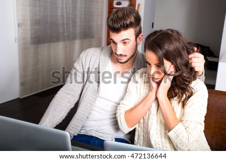 A young couple using in the evening their laptop computers at home and visiting a strange website.