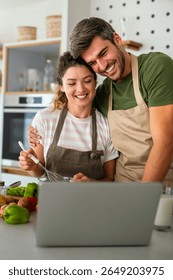 Young couple using laptop computer to take part in online culinary workshop, cooking together