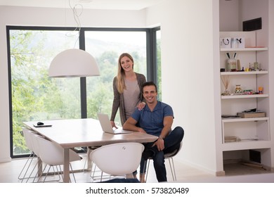 Young couple using laptop computer at luxury home together, looking at screen, smiling.
