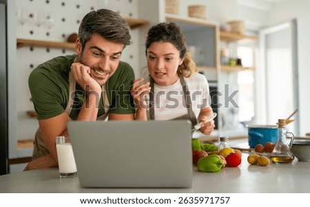 Young couple using laptop computer to take part in online culinary workshop, cooking together