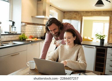 Young couple using a laptop in a kitchen at home - Powered by Shutterstock