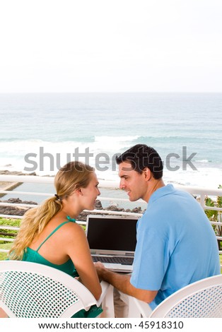 young couple using laptop on balcony, background is beautiful ocean view