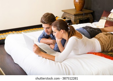 Young couple using a notebook in a asian hotel room while lying on the bed.